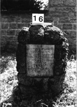 Grabstein 16 (Index: 100082098) Material: Granit, weiße Marmorplatte Zustand: Schriftplatte verwittert Maße HxBxT: 77x50x30 cm Beschreibung: Stele, rustica, rechteckige Schriftplatte Besonderheit: Zitat Jeremia 31, 20: Grabstein 16
