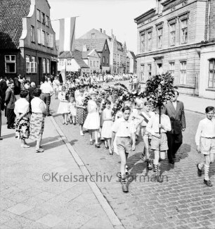 Kindervogelschießen: Umzug: Lübecker Straße: Jungengruppe mit Laubkranz, Mädchen mit Blumenbögen, Lehrer: an den Straßenrändern Zuschauer: an Fassaden Fahnenschmuck, 4. Juli 1957