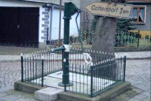 Pumpbrunnen mit schmiedeeisernem Zaun auf Platz beim Gemeindehaus