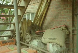 Mühlenstraße 10: Wassermühle: Detailaufnahme: Gebäudefront: unter Treppe zu Eingang: Zahnräder und Gestänge-Teile, Baumaterialien