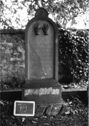 Grabstein 79 (Index: 100080579) Material: Sandstein Zustand: Stele mehrfach gesprungen Maße HxBxT: 143x43x20 cm Beschreibung: unterer Sockelteil rustica, Rundbogenabschl. mit Mittelakroter, Schrift eingetieft Symbolik: segnende Hände, Blätter mit Akroter Steinmetz: P. Müller: Grabstein 79