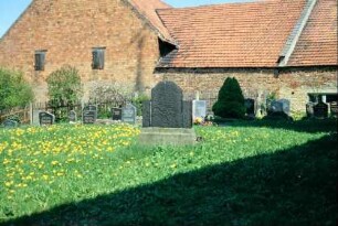 Friedhof mit Grabsteinen, daran angrenzend Bauernhof mit Backsteingebäude