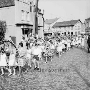 Kindervogelschießen: Umzug: Paul-von-Schoenaich-Straße: Mädchen mit Blumenbögen, Jungen mit Blumenstäben: Fahnenschmuck, Wimpelgirlanden über Straße: links "Fleischerei Bober", Zuschauer, 27. Juni 1964
