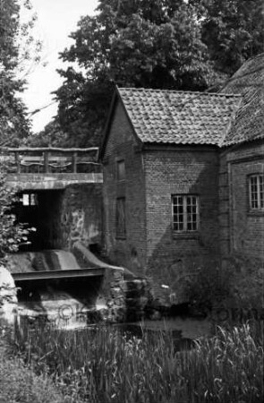 Glinder Mühle: rechts Mühlengebäude: links Mühlenwehr der Glinder Au: darüber Geländer: vorn Schilf: links und hinten Bäume