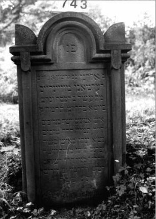 Grabstein 743 (Index: 99802192) Material: Sandstein Zustand: leicht verwittert/Textverlust Maße HxBxT: 117x62x22 cm Beschreibung: St. m. verdacht. eingezog. Rundbogen, Seitenakroterien, 2Halbsäulen Symbolik: Seitenakroterien, Halbsäulen Besonderheit: Endreim: Grabstein 743
