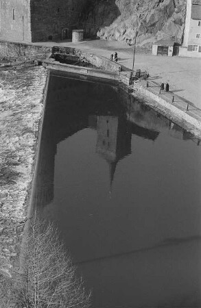 Blick auf ein Wehr, im Wasser spiegelt sich der Turm der Michaeliskirche