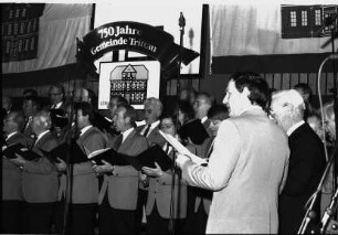 750. Gemeindejubiläum: Abschlussfeier: Sporthalle: Bühne: Männerchor beim Singen: Mikrofone, hinten Gemeindeflagge