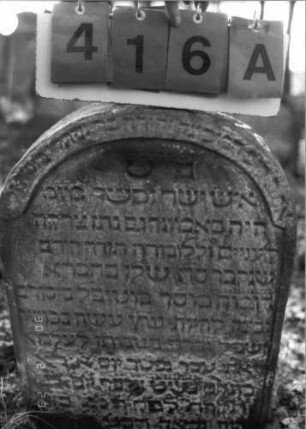 Grabstein 416 (Index: 100115650) Material: Sandstein Zustand: verwittert Maße HxBxT: 70x47x9 cm Beschreibung: Stele mit Rundbogenabschluß, eingetieftes Schriftfeld, weiteres Schriftfeld am Rundbogen Symbolik: Krone (des guten Namens) Besonderheit: kulturhistorisch wertvoll / hist.-wiss. Gründe (Gemeindestellung): Grabstein 416A (Detailaufnahme)