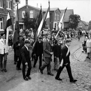 Kindervogelschießen: Umzug: ältere Schüler mit Fahnen: dahinter Festzug mit Blumenbögen: am Straßenrand Zuschauer, 15. Juli 1967