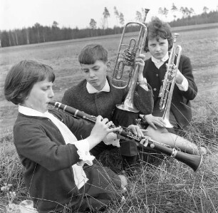 Drei Kinder mit Blasinstrumenten, auf einer Wiese sitzend