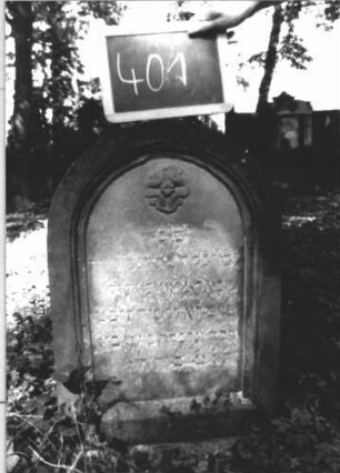Grabstein 401 (Index: 100111819) Material: Sandstein Zustand: stark verwittert mit Textverlust Maße HxBxT: 68x46x14 cm Beschreibung: Stele, Rundbogenabschluß, Schriftfeld eingetieft Symbolik: Blüte Besonderheit: Kindergrab: Grabstein 401