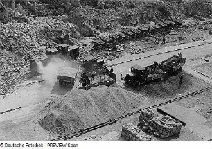 Dresden. Blick auf eine Baustelle zwischen Trümmern, Kipplorenzug der Trümmerbahn wird beladen - Lastkraftwagen mit Baustoffen werden entladen