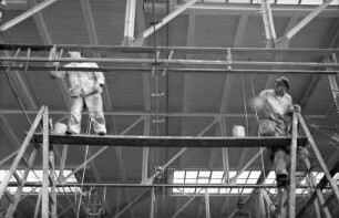 Radebeul-Kötzschenbroda, wohl Fabrikstraße 27. Elektroarmaturenwerk JWH. Fabrikhalle. Zwei Maler beim Streichen von Rohren