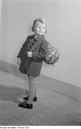 Ein Mädchen mit einem Ball in einem Ballnetz präsentiert Kinderbekleidung