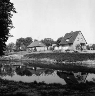 Neubausiedlung: vorn Teich: dahinter mehrere Einfamilienhäuser mit Gärten: dahinter Bäume