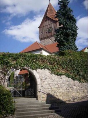 Ansicht von Südwesten mit Kirche über Kirchhofmauer mit erhaltenem Außenbogen des ehemaligen Kammertors (Wehrgang mit Steinbrüstung sowie Toranlage im 18 Jh abgetragen)