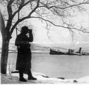 Soldat mit Fernglas vor zerstörtem Schiff