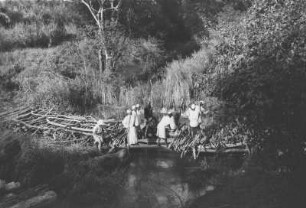 Bau der Mbenkuru-Notbrücke bei Kitumbini : Landschaft mit Arbeitern beim Bau einer einfachen Brücke über einen Fluss