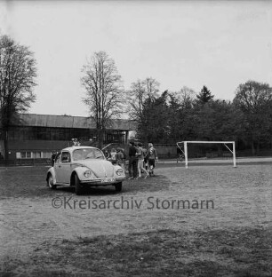 Exer: parkender VW Käfer neben Sportplatz: rechts dahinter Kinder beim Sport: hinten links Stormarnhalle
