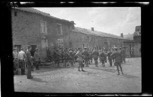 Bei Mouzon (?) (Dep. Ardennes, Frankreich): Regimentsmusik auf einem Ortsplatz vor einer niedrigen Häuserzeile (Distanzaufnahme)