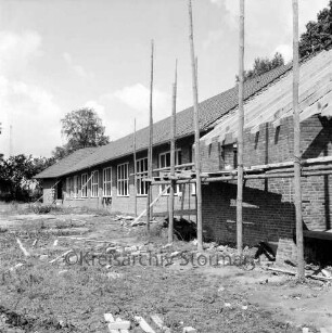 Volksschule: Schulkoppel: Neubau vor Fertigstellung: vorn rechts Turnhalle im Rohbau mit Gerüst: hinten Bäume: vorn Baumaterial