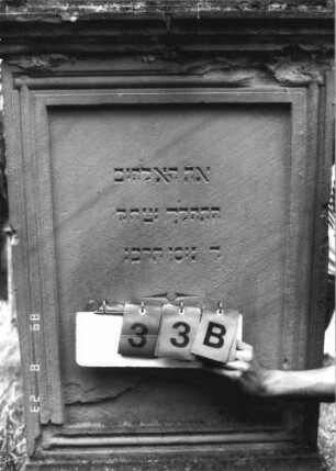 Grabstein 33 (Index: 100110895) Material: Sandstein Zustand: stark verwittert im Giebel, Abschieferungen im unteren Teil Maße HxBxT: 166x75x28 cm Beschreibung: Stele, Sockel, Rundbogenabschluß mit Zahnradfries und Verdachung, Schriftfelder eingetieft: Grabstein 33B