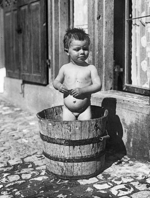 Bei großer Hitze ist das Baden aber schön! Kleines nacktes Mädchen beim Baden in einem Holzbzuber