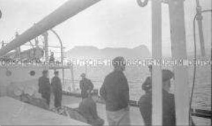 Heimfahrt der Kriegsgefangenen vom Internierungslager "Angel Island" auf dem italienischen Dampfer "Fella", mehrere Personen an Deck, bei Sonnenuntergang gen Felsenküste blickend