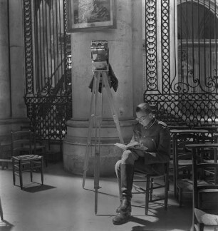 Der lesende Franz Prinz zu Sayn-Wittgenstein neben einer Kamera im Chorumgang der Kathedrale Saint-Julien in Le Mans (Aufnahme im Rahmen der Fotokampagne im besetzten Frankreich)