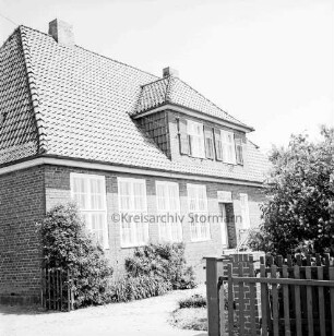 Volksschule: vorn rechts Zaun: dahinter Büsche