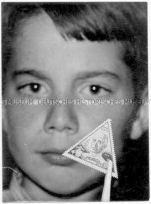 Gesicht eines Jungen, im Vordergrund eine Pinzette mit Briefmarke