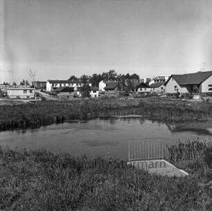 Kurpark: Teich, vorne ein Steg mit Geländer, im Hintergrund Wohngebäude