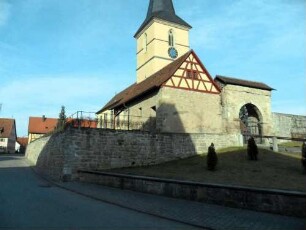 Ansicht von Ostsüdosten mit Kirche (im Kern Romanisch 12 Jh) über Kirchhofmauer und Romanischem Torbogen-Wehrgang der Kirchhofmauer mit Steinbrüstung sowie Torhaus im 18 Jh weitgehend abgetragen