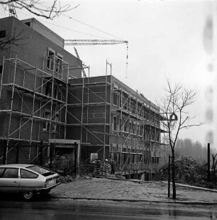 Kreiswehrersatzamt: Berliner Ring: in Bau: Richtfest: Rohbau mit Gerüst, hinten Richtkrone: Baukran: Bauzaun, Stapel mit Holzplanken, Personen: vorne an Straße parkender Pkw, junger Baum, 11. Dezember 1980