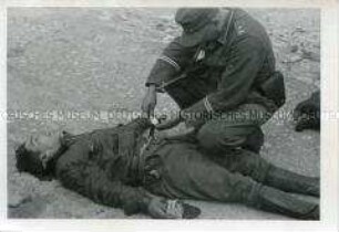Ein Stabsfeldwebel der Wehrmacht beim Durchsuchen eines getöteten französischen Widerstandskämpfers