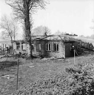 Rögen: Brand: Reetdachkate: Ruine mit eingestürztem Dachstuhl: davor Baum: links Feuerwehrmann beim Löschen: rechts Feuerwehrmann an Fenster: Wasserstrahl einer Feuerwehrspritze