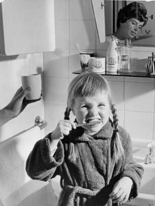 Ein kleines Mädchen putzt sich im Bad die Zähne. Ihre Mutter schaut zu und kontrolliert. Werbeaufnahme für die Techniker Krankenkasse (TK)