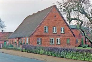 Hauptstraße (17-19): Hofanlage: traufständiges Haupthaus, Backsteingebäude: Straßenfront, von links Wirtschaftstrakt, Eingangstür, Wohntrakt: Giebelseite Wohntrakt: rechts rückwärtiger Wirtschaftsquerbau: hinten Nebengebäude: vorne Grundstückszaun, Hecke, Garten