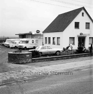 Firma Günter Kropp: Lebensmittelvertrieb: Bolande: Außenansicht: Betriebsgelände mit Einfahrt, Bürogebäude, Verkaufs- und Lagerhalle, mit Firmenlogo: Verkaufsfahrzeuge "rollender Kaufladen" in Reihe, mit Firmenaufschrift "Kropp - im Dienste der Hausfrau": Arbeiter im Vorgarten, Junge auf Gartenmauer