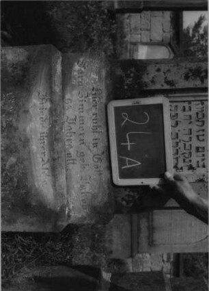 Grabstein 24 (Index: 99801893) Material: Sandstein Zustand: verwittert Maße HxBxT: 144x47x22 cm Beschreibung: ädikulaartige Stele mit Pilastern, getreppter Sockel, geschwungener giebelartiger Abschluß mit Verdachung, eingetietes Schriftfeld mit Rundbogen Besonderheit: seltene Form: Grabstein 24A