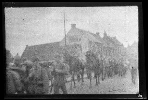 Nicht identifizierbare Ortschaft in Nordfrankreich oder Belgien: 2 Reiter zwischen Soldaten mit Pickelhaube auf einer gepflasterten Ortsstraße