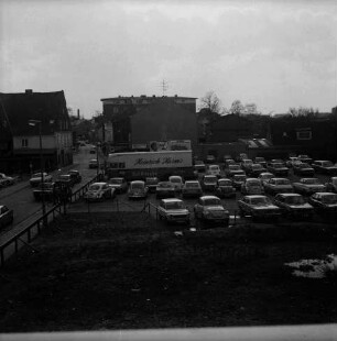 Hagenstraße / Weg am Bürgerpark: eingezäunter Baugrund für Neubau der Kreissparkasse Stormarn: Parkplatz mit Lkw der Firma Heinrich Harms und Pkws: dahinter Werbeplakatwand und Wohn- und Geschäftshäuser: 19. April 1975