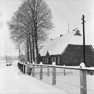 Bauernhaus: davor Baumreihe; Strommast und Zaun: hinten links Pkw: dahinter Häuser: Winter
