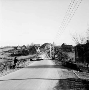 Dorfstraße: Landesstraße zwischen Reinfeld und Westerau: vorn links Fußgängerin: hinten Mitte Bus: rechts Strommasten: dahinter und hinten Häuser: Blick auf den Ort