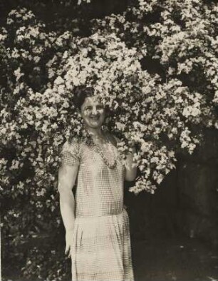 Der Frühling ist da. Eine Frau steht in einem blühenden Strauch. Ihr scheint die Sonne in´s Gesicht