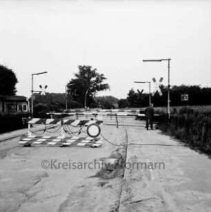 Bahnübergang Am Weinberg: Schranken geschlossen, Andreaskreuze, Straßenlampen, Spiegel: Fahrradfahrer wartet: im Vordergrund Absperrschranke: links Schrankenwärterhäuschen: Blick Richtung Schlosspark