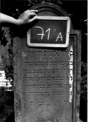 Grabstein 71 (Index: 100109955) Material: Sandstein Zustand: verwittert Maße HxBxT: 145x42x17 cm Beschreibung: Stele, getreppter Sockel, eingezogener Rundbogenabschluß, Schriftfeld eingetieft: Grabstein 71A