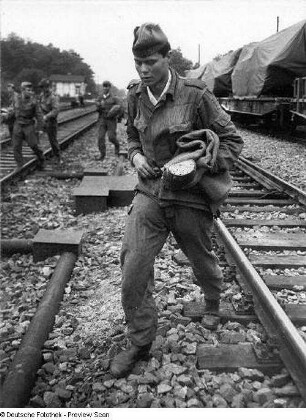 Deutschland . Truppenübungsplatz Klietz. Nationale Volksarmee - Landstreitkräfte. Truppenverlegung per Eisenbahnmarsch. Soldaten überqueren Gleise neben einem Militärzug