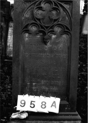 Grabstein 958 (Index: 99802656) Material: Sandstein Zustand: leicht verwittert Maße HxBxT: 210x57x45 cm Beschreibung: mehrfach getreppter Sockel, Stele mit verdachtem Giebel Symbolik: Inschriftenfeld mit gotisierendem Maßwerk: Grabstein 958A