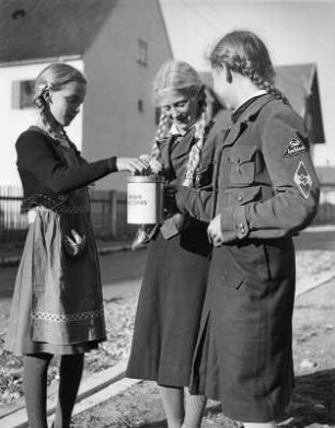 BdM (Bund Deutscher Mädel). Zwei Mädchen in BdM-Uniform mit Sammelbüchse für das Winterhilfswerk, ein Mädchen in Zivil beim Eiwerfen der Spende